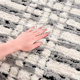 Close-up of the textured Nava Area Rug in beige, black, and bone with a geometric pattern. Hand touching the soft pile. Texture
