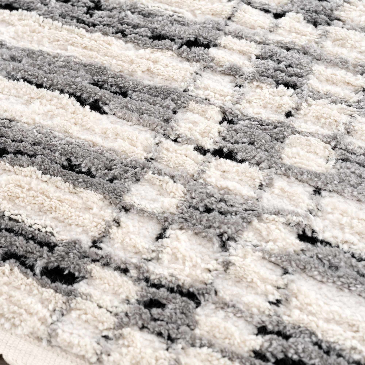 Close-up of the Nava Area Rug. Beige, bone, and black geometric pattern. Soft, textured, machine-woven pile. Texture