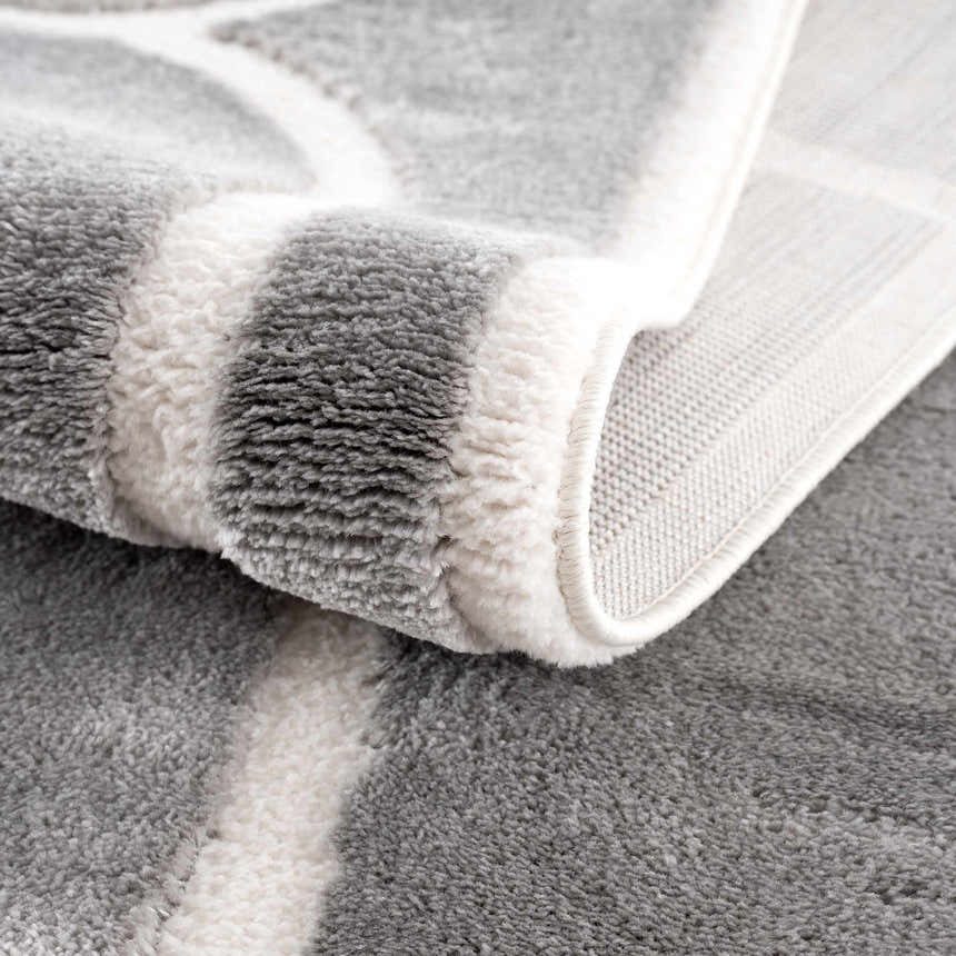 Close-up of the plush texture and geometric pattern of the gray and cream Azana Modern Area Rug. Fold