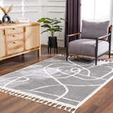 Living room scene with gray armchair and Azana Modern Gray Area Rug with abstract white pattern and tassels. Roomscene-Rectangle