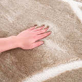 Close-up of the plush texture of the cream Azana Area Rug with a hand pressing into the soft, geometric design. Texture