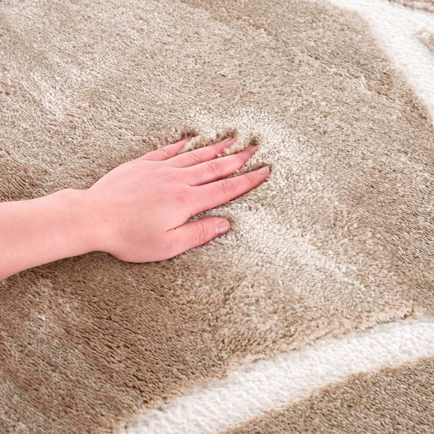 Close-up of the plush texture of the cream Azana Area Rug with a hand pressing into the soft, geometric design. Texture