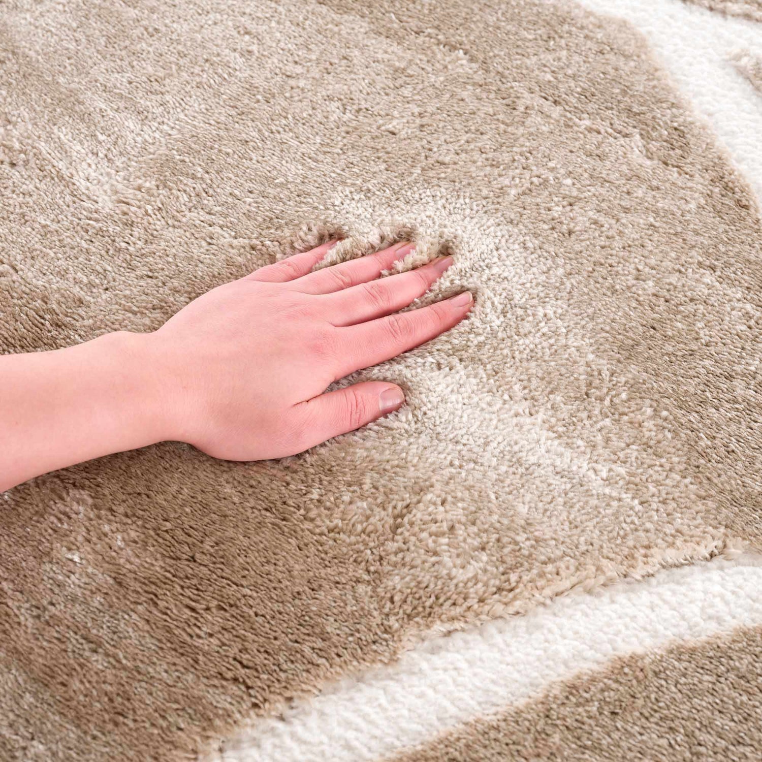 Close-up of the plush texture of the cream Azana Area Rug with a hand pressing into the soft, geometric design. Texture