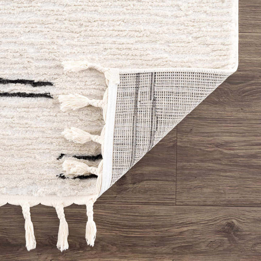 Close-up of the Riad Black Striped White Rug with Tassels showing texture, black stripes, tassels, and rug backing. Fold