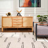 Living room scene with a Riad Black Striped White Rug, wood cabinet, gray chair, and colorful art. Roomscene-Rectangle