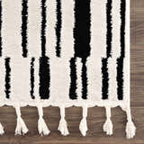 Close up of the Bansi Area Rug, showcasing its black and beige geometric pattern and tasseled edge. Swatch
