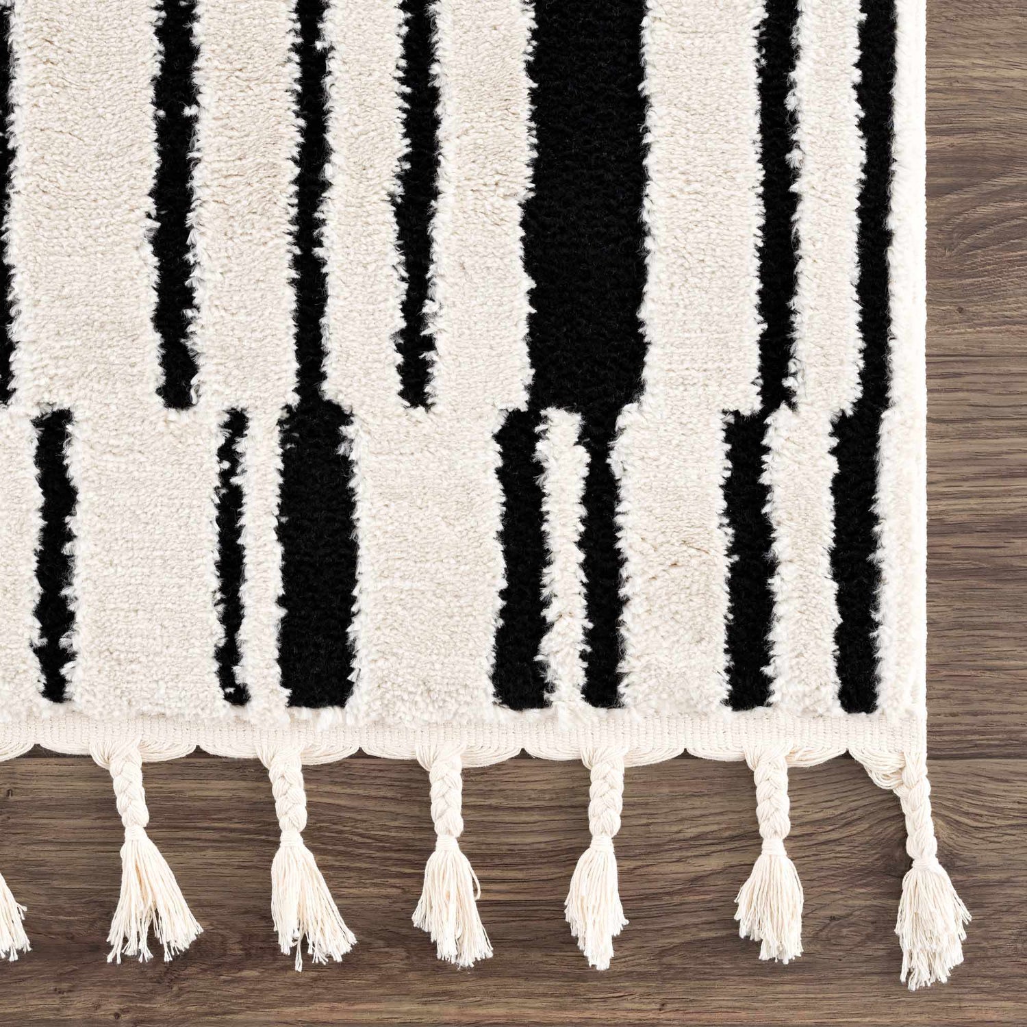 Close up of the Bansi Area Rug, showcasing its black and beige geometric pattern and tasseled edge. Swatch