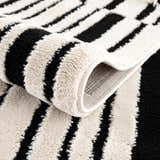 Close-up of the Bansi Area Rug. Beige and black stripes with a plush, textured pile. Machine woven construction. Fold