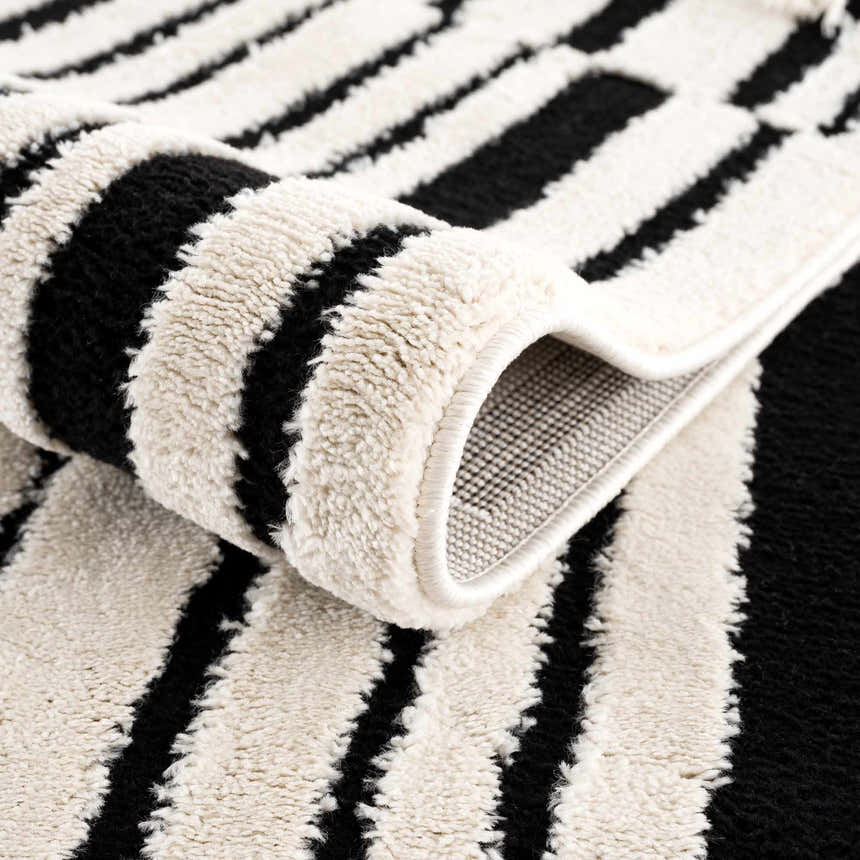 Close-up of the Bansi Area Rug. Beige and black stripes with a plush, textured pile. Machine woven construction. Fold