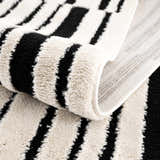 Close-up of the Bansi Area Rug showing its beige and black geometric stripe pattern and plush, machine-woven texture. Fold