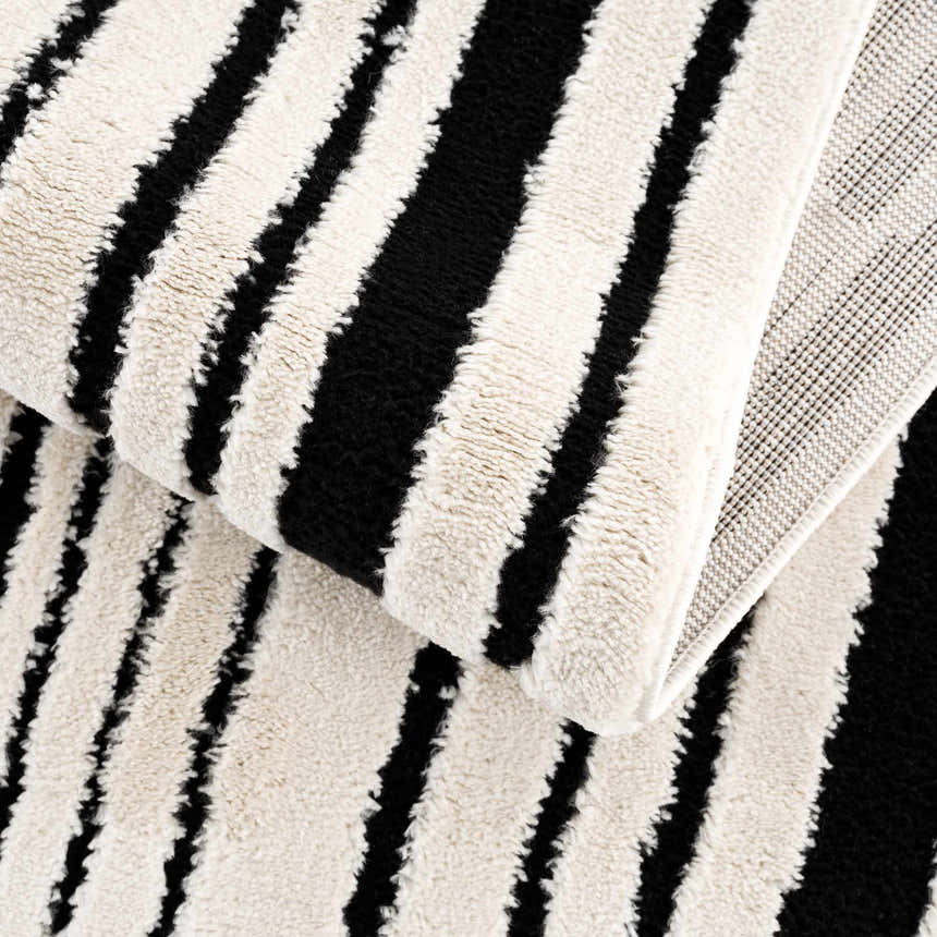 Close-up of the Bansi Area Rug: beige and black stripes, plush texture, machine woven construction. Fold