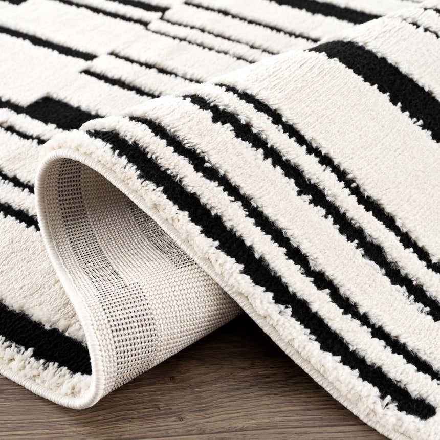 Close-up of the Bansi Area Rug showing its geometric black and bone pattern and textured polypropylene weave. Fold