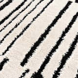 Close-up of the Bansi Area Rug: a machine-woven rug with a geometric pattern in beige and black. Soft, textured polypropylene. Texture