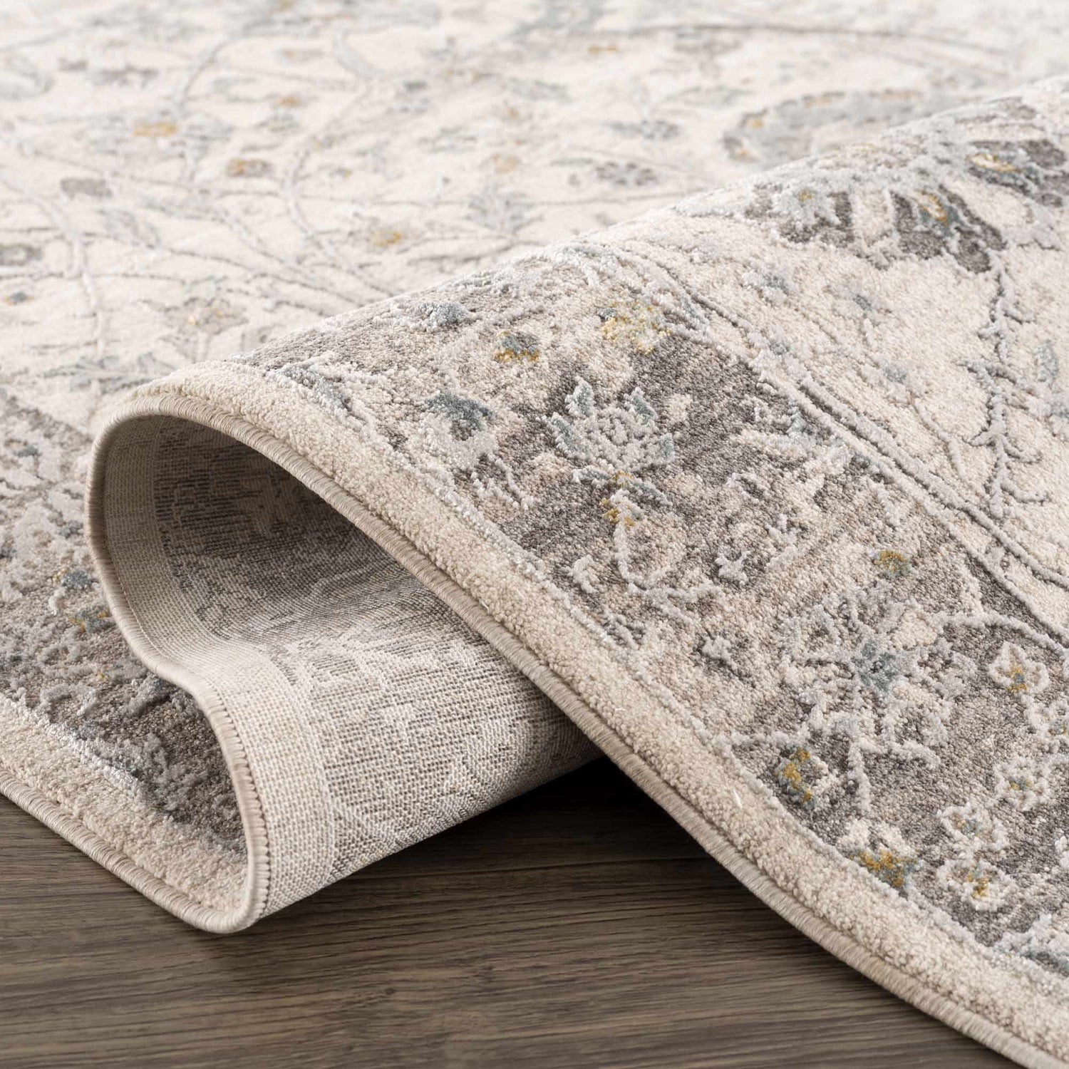 Close-up of the Gauge Cream & Gray Blue Rug showing its traditional floral pattern and soft, textured weave. Fold