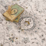 Close-up of Gauge Cream & Gray Blue Rug showing traditional floral pattern and soft texture. Stack of books on rug. Styleshot