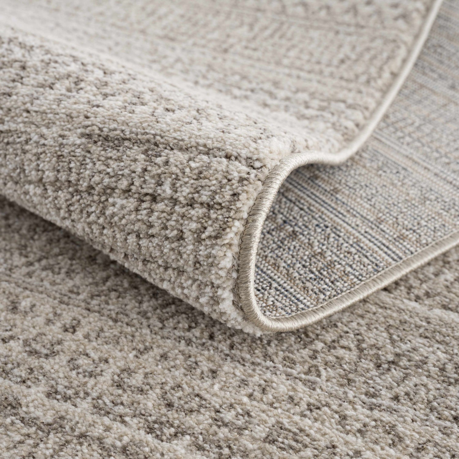 Close-up of the Nate Beige Tribal High Pile Carpet showing its texture, neutral colors, and machine-woven construction. Fold