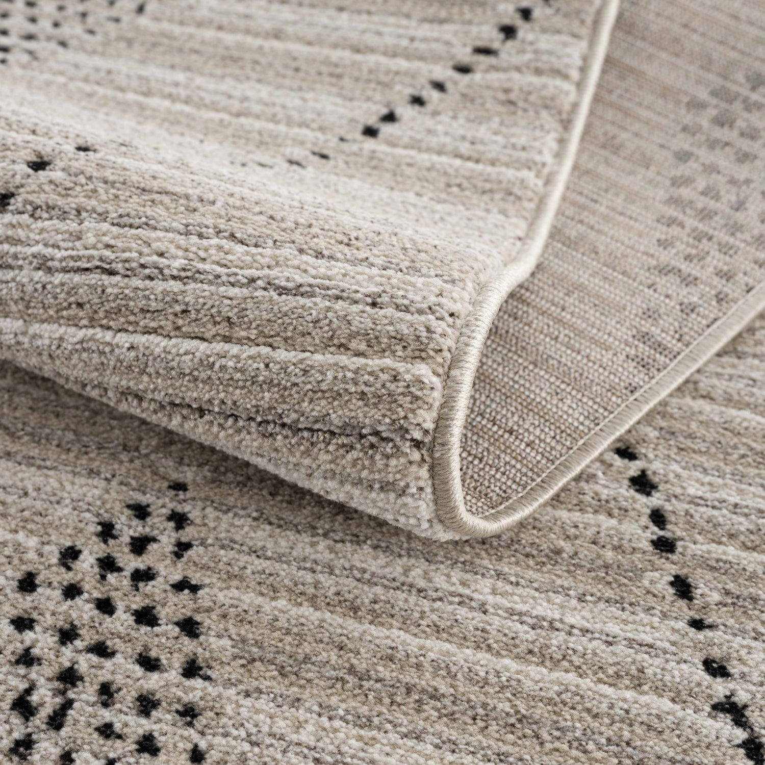 Close-up of the Lexi Area Rug showing its beige and ivory geometric pattern and soft, textured polyester pile. Fold