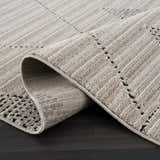 Close-up of the Lexi Area Rug, a beige and ivory geometric rug made of polyester, rolled up to show texture. Fold