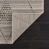 Close-up of the Lexi Area Rug. Beige and ivory rug with a geometric design on a dark wood floor. Rug backing visible. Fold