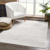Living room scene with Tigri Aztec Ivory & Gray rug, white armchair, woven ottoman, and plant near a bright window. Roomscene-Rectangle