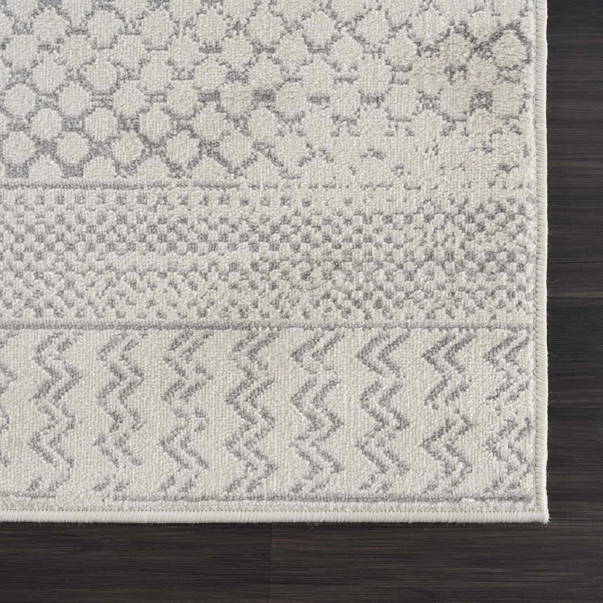 Close-up of Tigri Aztec Ivory & Gray rug showing geometric patterns and soft texture on dark wood floor. Corner