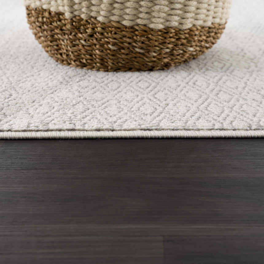 Close-up of Tigri Aztec Ivory & Gray rug with a diamond pattern and a woven basket on dark wood floor. Pile
