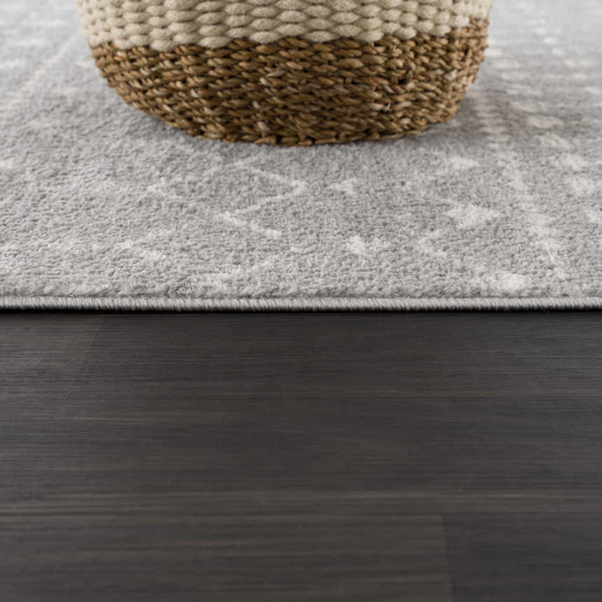 Close-up of the Tigrican Light Gray rug showing its soft texture and subtle ivory pattern with a woven basket on top. Styleshot