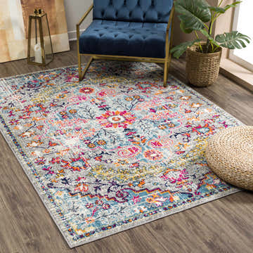 Living room scene with a Delanson Colorful Area Rug, blue velvet chair, and woven pouf. Roomscene-Rectangle