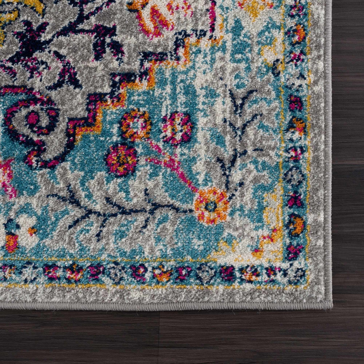 Close up of the New Delanson Area Rug, showcasing its floral, traditional pattern in gray, teal, pink, and yellow. Corner
