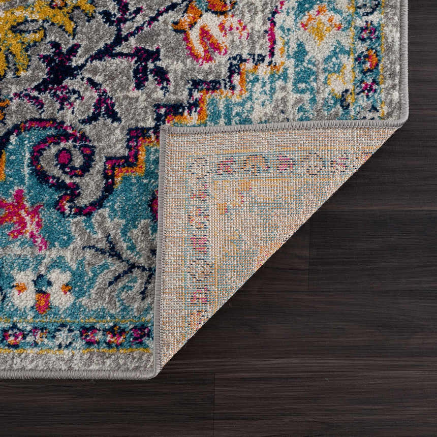 Close-up of New Delanson Area Rug showing floral pattern in gray, teal, yellow, and pink on dark wood floor. Fold