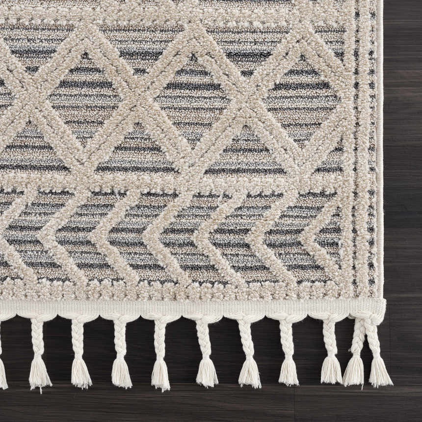 Close-up of Magnolia Cream 2300 Area Rug showing geometric pattern, soft texture, and braided fringe detail. Beige, cream, and smoke colors. Swatch