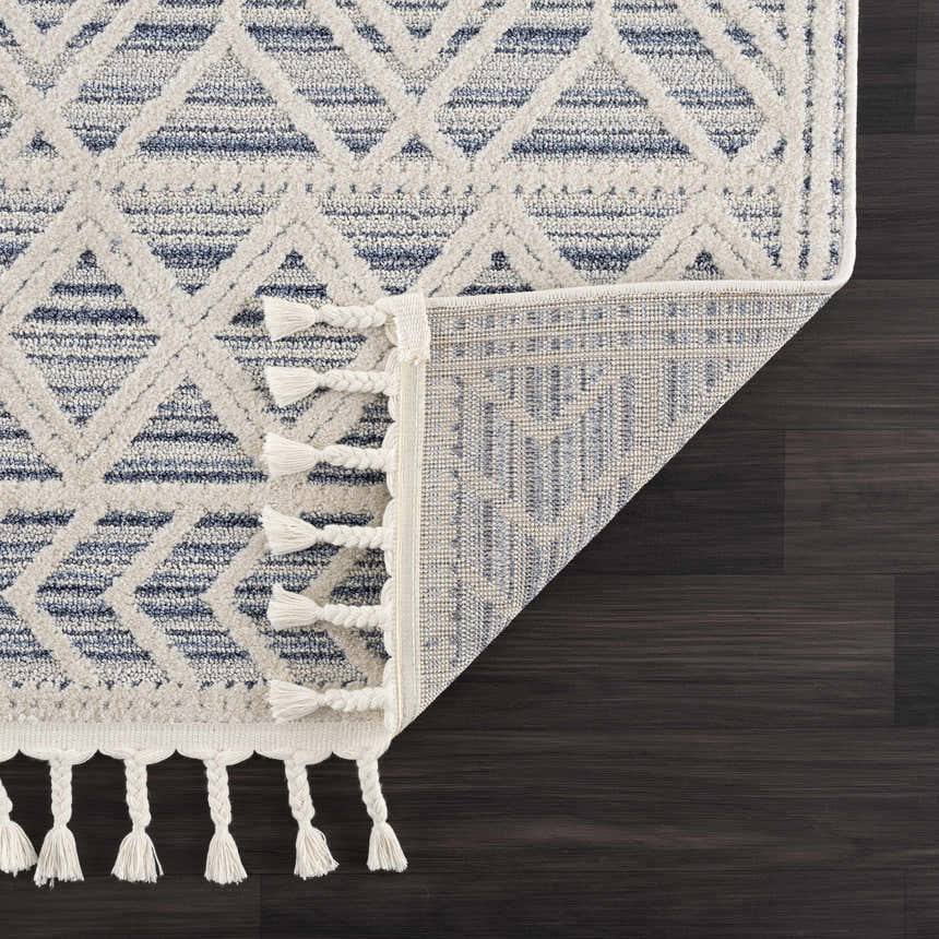 Close-up of Magnolia Blue 2302 Area Rug showing geometric pattern, cream and blue colors, tassels, and machine-woven construction. Fold