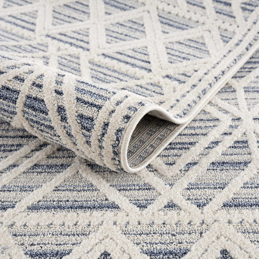 Close-up of the Magnolia Blue 2302 Area Rug showing cream and dark blue geometric pattern and soft, textured polypropylene pile. Fold