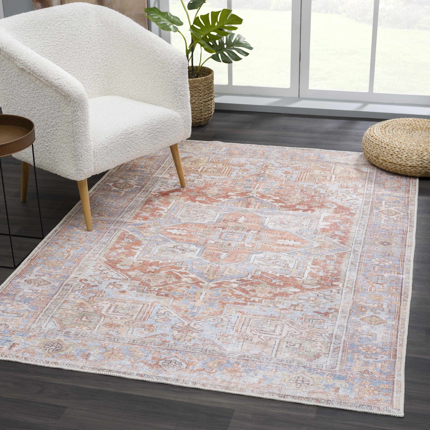 Living room scene with a Rust Maayon Washable Rug, white chair, side table, and woven ottoman. The rug has a vintage, oriental design. Roomscene-Rectangle