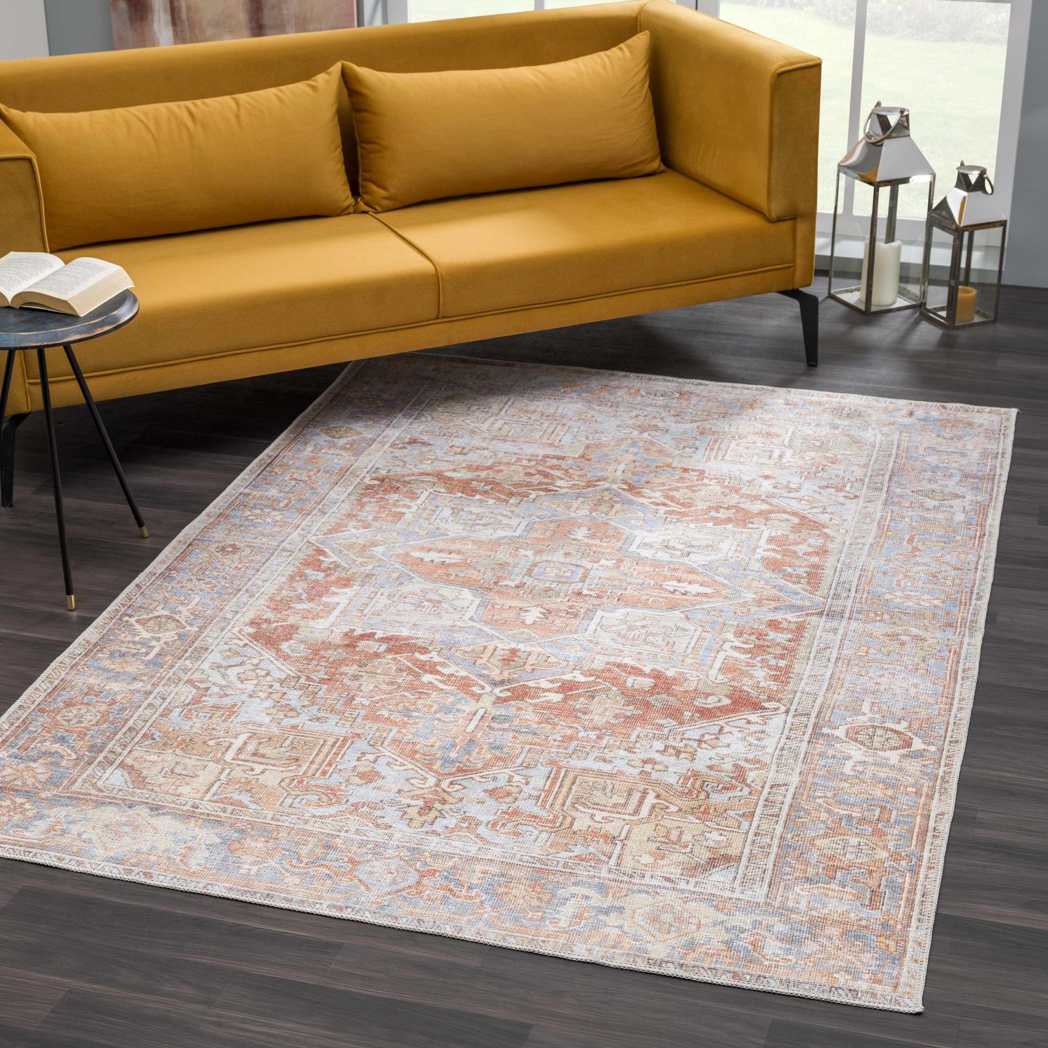 Living room scene with a Rust Maayon Washable Rug, mustard sofa, dark wood floors, and silver lanterns. Roomscene-Rectangle