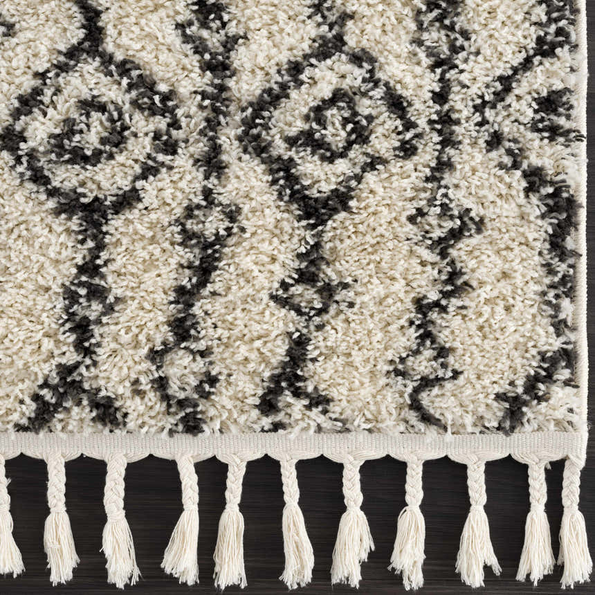 Close up of the Bayanga area rug, a shag rug with a gray Aztec pattern and white tassels. Swatch