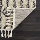 Close-up of the Bayanga area rug showing the shag texture, gray Aztec pattern, tassels, and woven backing. Fold