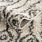 Close-up of the Bayanga area rug showing its charcoal and ivory shag texture and woven backing. Fold