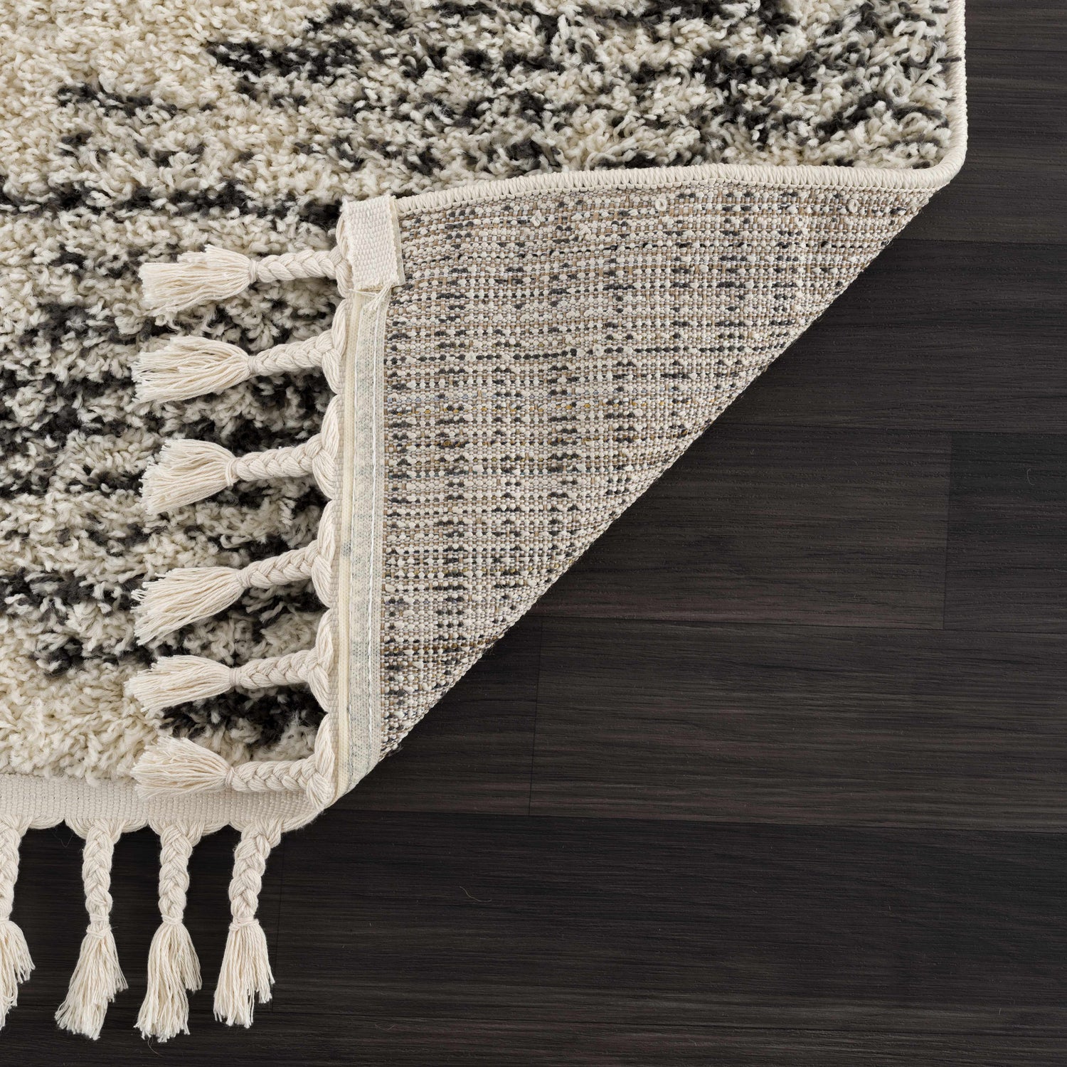 Close up of the Howth Area Rug showing bone and dark gray shag texture and braided tassels. Corner