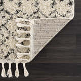 Close-up of the Kibureau Area Rug showing the beige and charcoal shag texture, tassels, and machine-woven backing. Fold