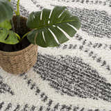 Close-up of the Trunding Plush Area Rug in charcoal and cream with a bohemian-inspired pattern and a potted monstera plant. Styleshot