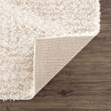 Close-up of the Hauteloom Trunding Plush Rug in Light Beige showing its shag texture and durable backing on a wood floor. Fold