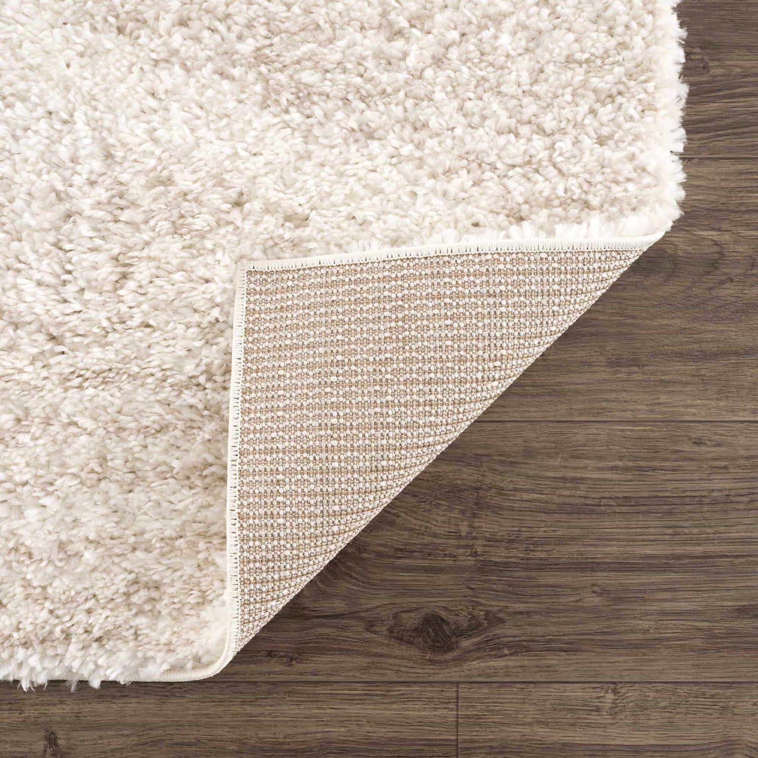 Close-up of the Hauteloom Trunding Plush Rug in Light Beige showing its shag texture and durable backing on a wood floor. Fold