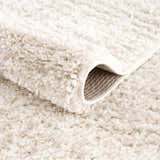 Close-up of the Hauteloom Trunding Plush Rug in Light Beige. Shows the shag texture and woven backing detail. Fold
