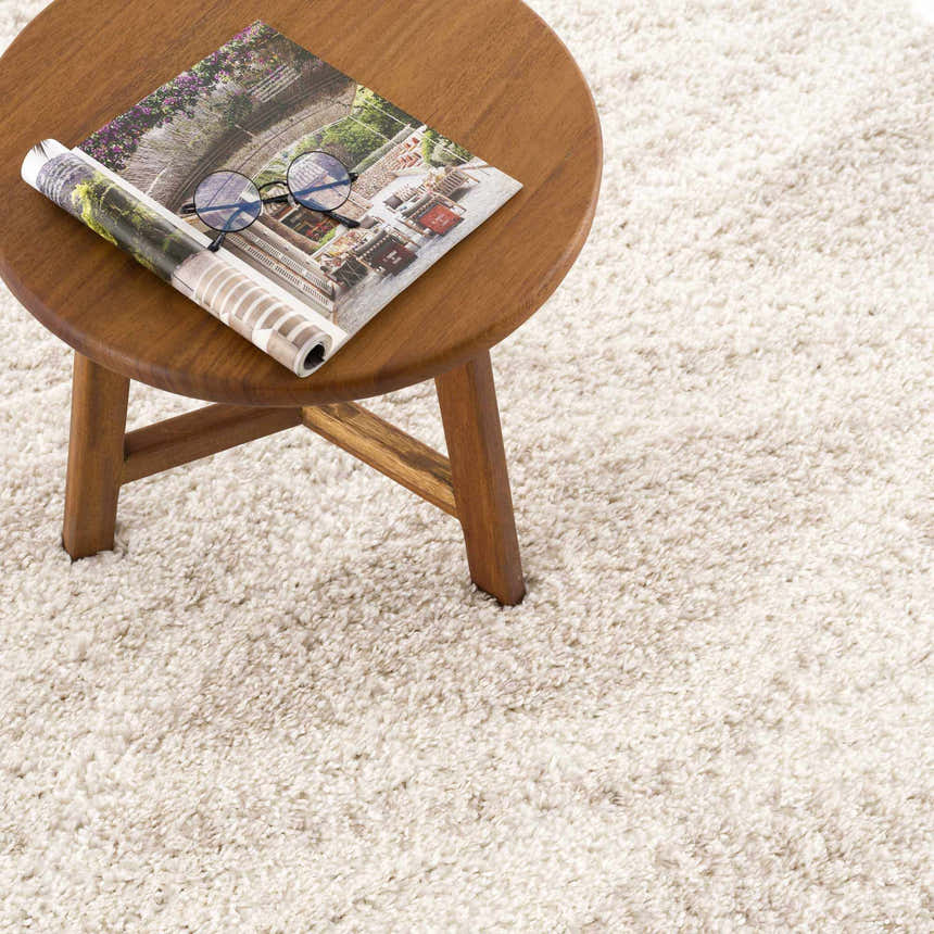 Close-up of the plush texture and light beige color of the Hauteloom Trunding rug, with a small wood table. Styleshot