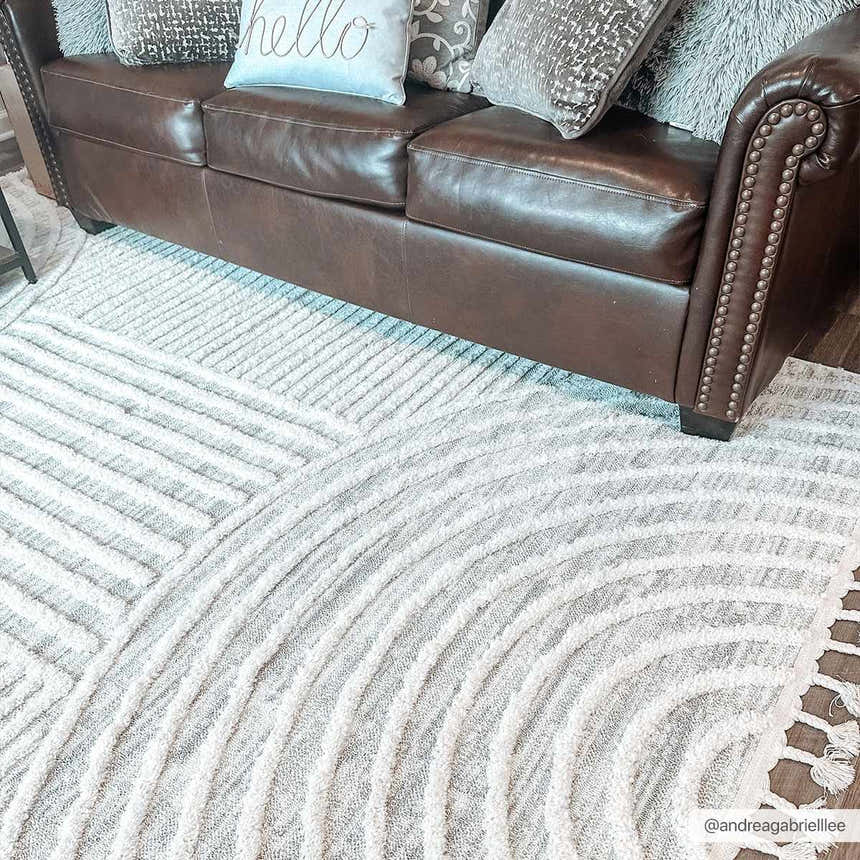 Living room scene with brown leather sofa and Dauin 3D Rainbow Area Rug. Gray and cream geometric pattern with tassels. Roomscene-Rectangle