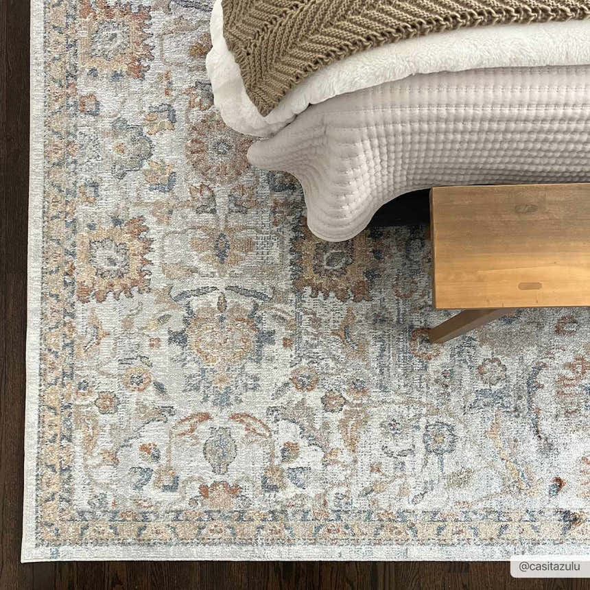 Bedroom scene with Dion Washable Floral Rug in charcoal, beige, and blue. Farmhouse style with bed and wooden bench. Roomscene-Rectangle