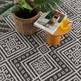 Close-up of Frankville Black&White All Over Performance Rug with geometric pattern, plant, magazine, and drink on a table. Styleshot