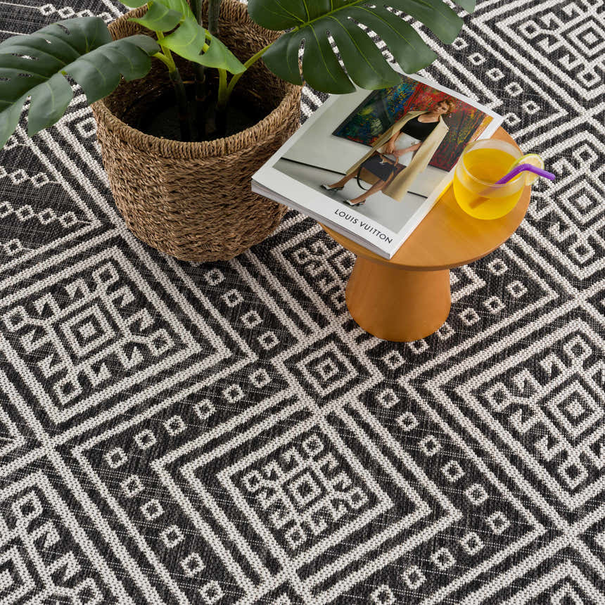 Close-up of Frankville Black&White All Over Performance Rug with geometric pattern, plant, magazine, and drink on a table. Styleshot
