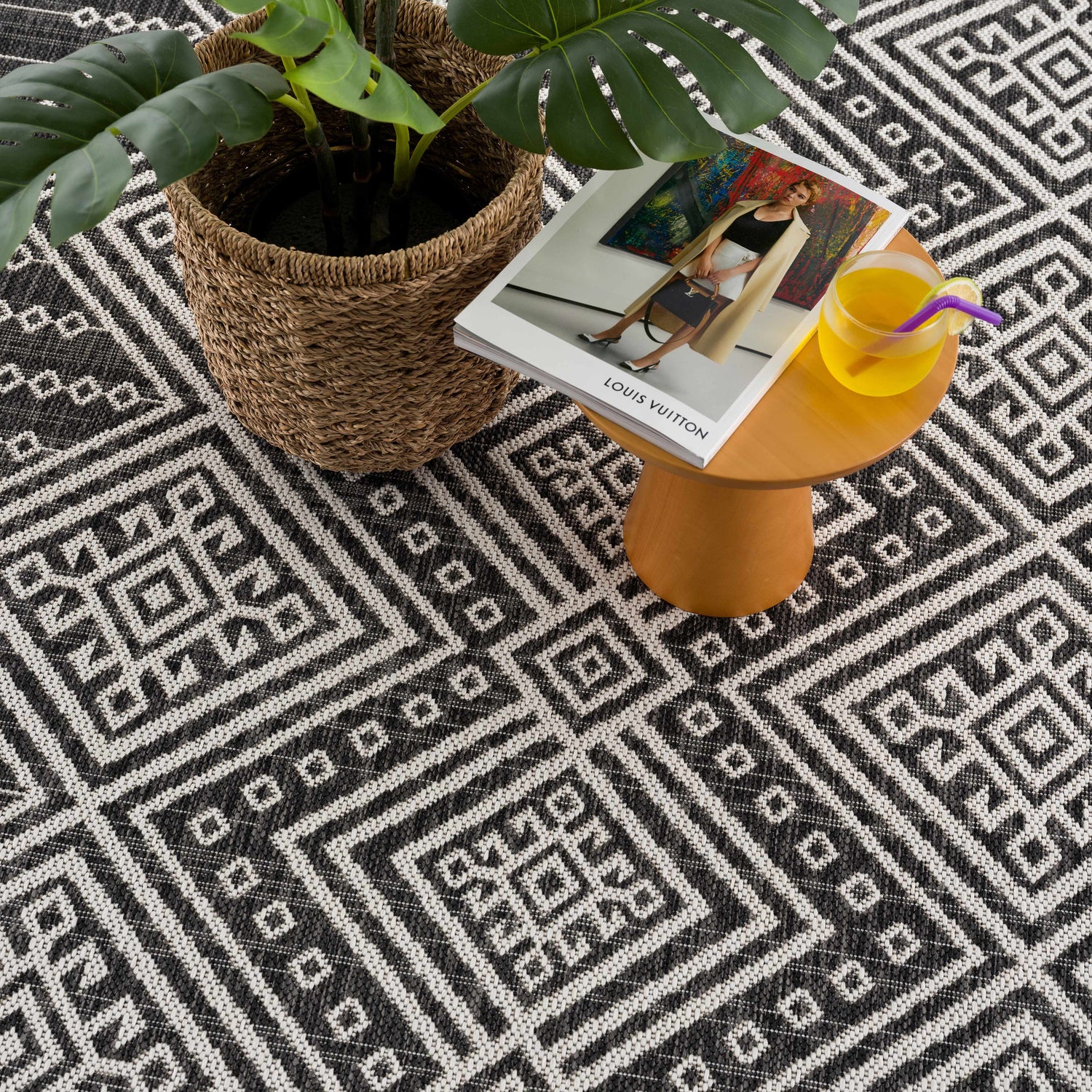 Close-up of Frankville Black&White All Over Performance Rug with geometric pattern, plant, magazine, and drink on a table. Styleshot